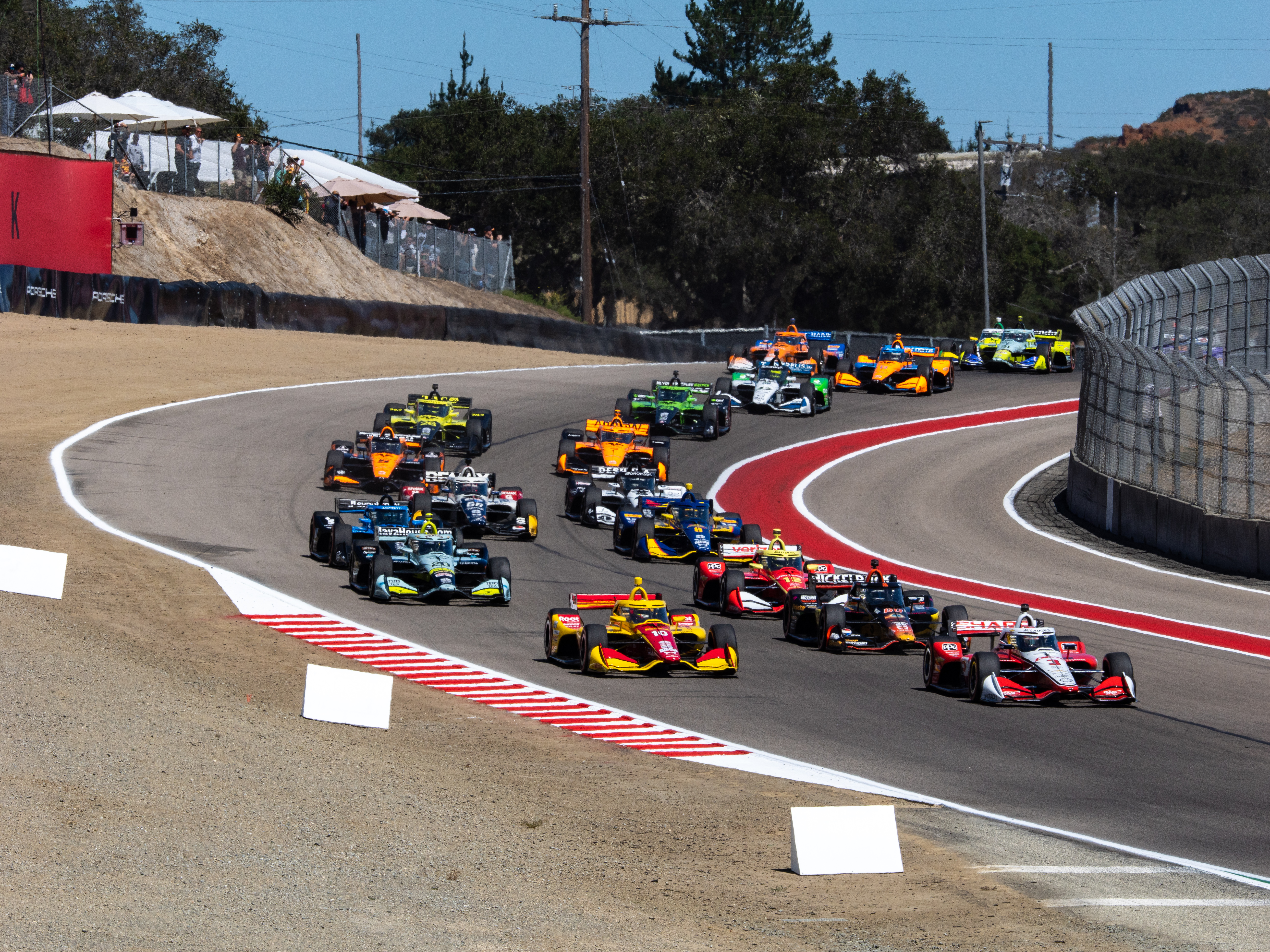 IndyCar field racing over the hills at WeatherTech Raceway Laguna Seca.